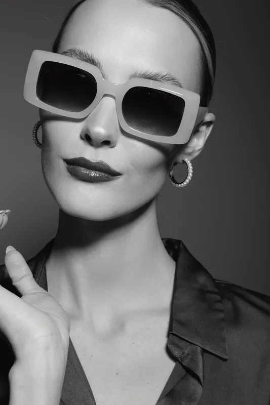 Portrait of a young white woman with pale skin wearing large sunglasses and hoop earrings in black and white. Fashion concept with confident expression and stylish look.