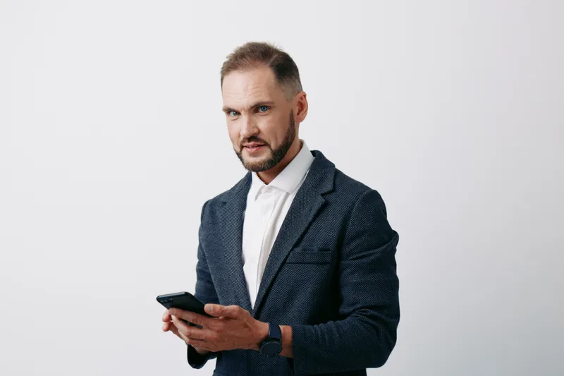 A focused business professional man stands against an isolated colored background, checking a smartphone with intent. Confident, thoughtful, and composed in a modern corporate pose.