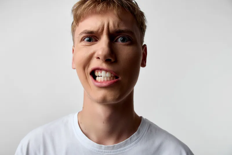 Closeup of an angry, frustrated man with clenched teeth and wide eyes, conveying intense emotion, discomfort, and a moment of vehemence suitable for reaction, confrontation, or stress themes