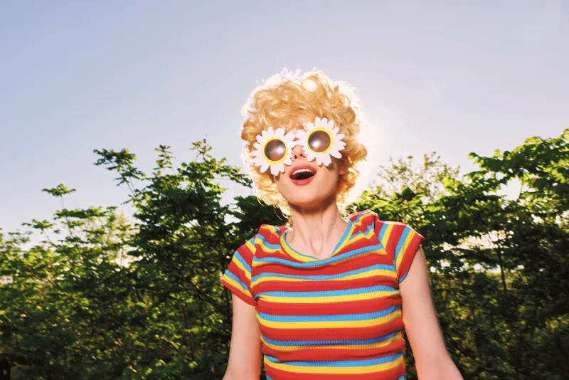 A woman in a striped top with sunflower sunglasses in a sunny outdoor scene. A bright retro vibe conveys playful summer mood and carefree lifestyle.