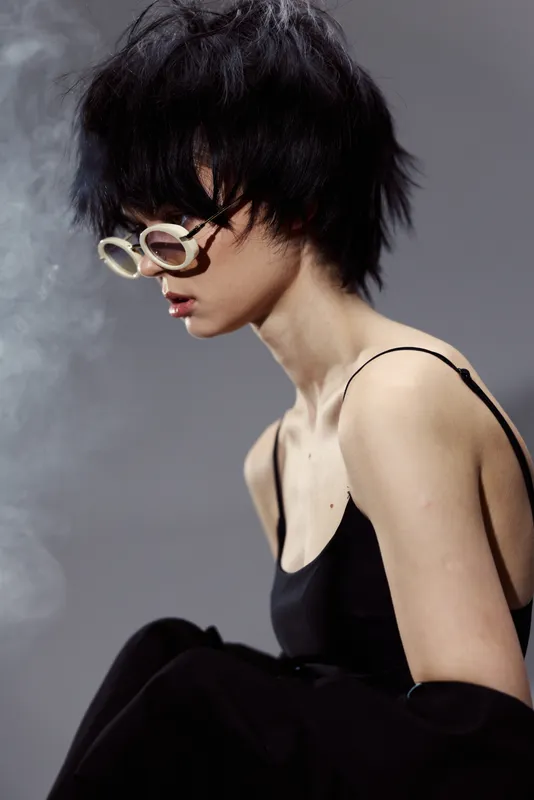 young woman with short black hair and stylish glasses wearing black top in smoky atmosphere