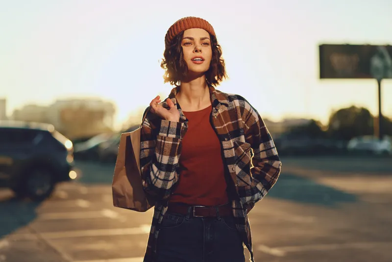 Woman shopping on a street in an urban scene, candid portrait capturing authenticity and confident style with a golden glow at golden hour, wearing a beanie and plaid jacket.