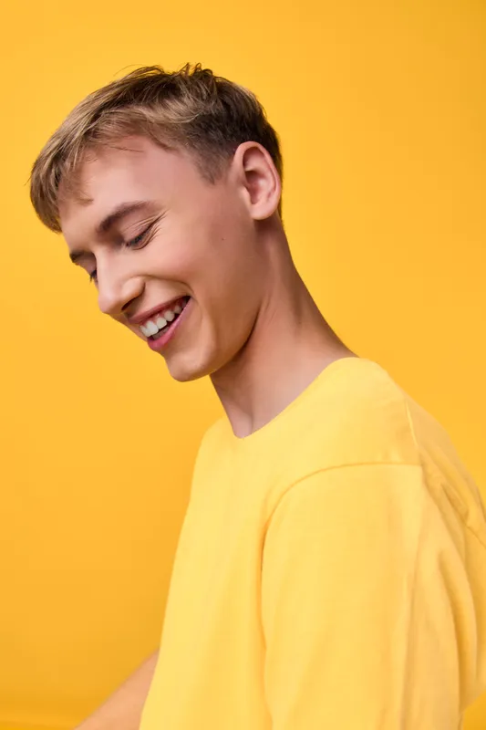 Smiling young man in a bright yellow shirt against a vivid yellow background, exuding cheerful energy, warmth and positivity for lifestyle and fashion concepts