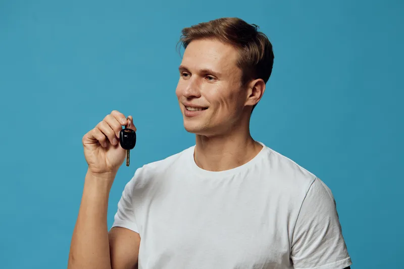 smiling man holding car keys blue background casual white t-shirt digital nomad concept technology autonomy