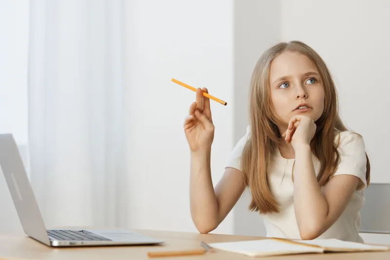 Thoughtful girl studying at home with a laptop she is deep in thought, holding a pencil, in a bright, minimalistic setting