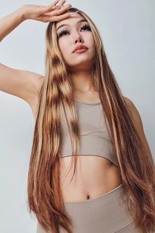Young woman with long straight hair and natural makeup posing in beige sporty top and bottom on light background. Fashion, beauty, lifestyle and fitness concept with confident model.