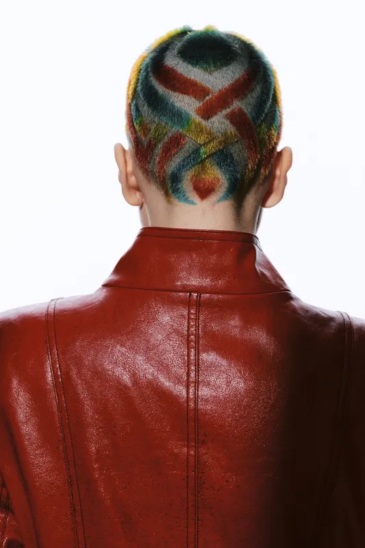 Woman with colorful short hair design viewed from behind, wearing a red leather jacket, showcasing creative fashion and unique hairstyle details.