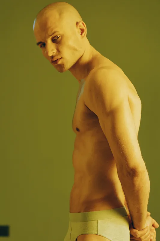 Portrait of a confident man, showcasing strong physique and natural beauty under soft lighting. The image captures a moment of self-reflection, exuding strength and determination.
