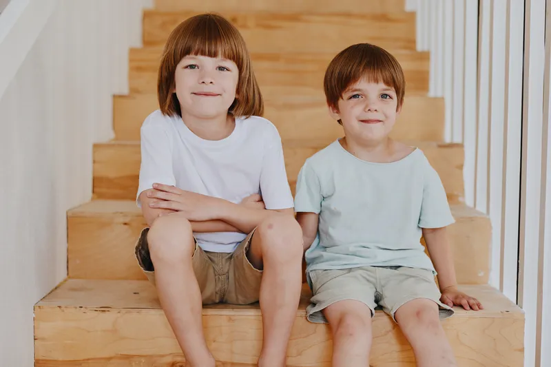 Two cheerful boys sit on wooden stairs, enjoying their time together. They display a playful spirit with light clothing and friendly expressions.
