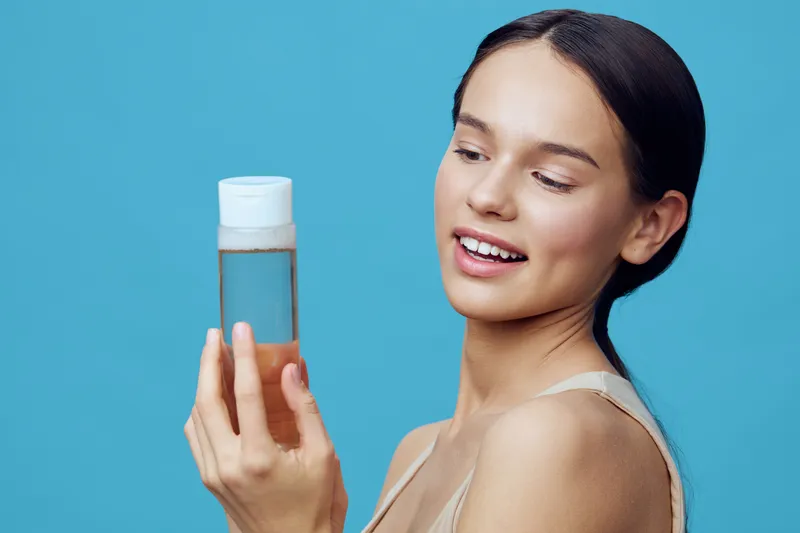 Young woman admiring a skincare product in a minimalistic setting, showcasing beauty and self care with a light blue background and natural makeup