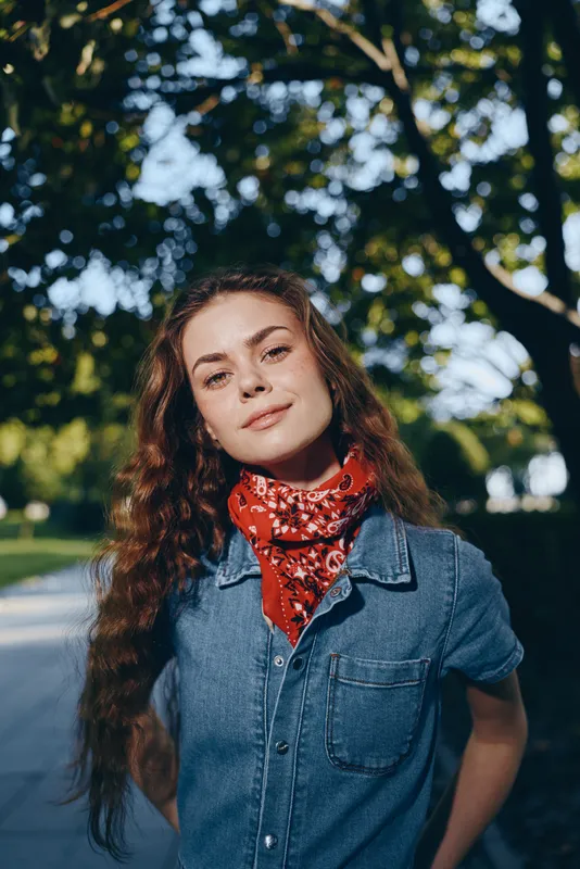 Lifestyle woman in modern boho-western denim street style with a red bandana, natural light, and film color capturing a confident outdoor look.
