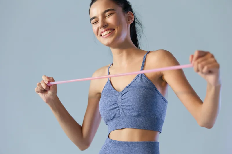 young woman sport fitness stretching with resistance band in casual blue activewear, smiling with eyes closed, healthy lifestyle and exercise concept