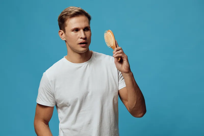 young caucasian man in white tshirt holding hairbrush look away thoughtful casual style blue background digital detox concept