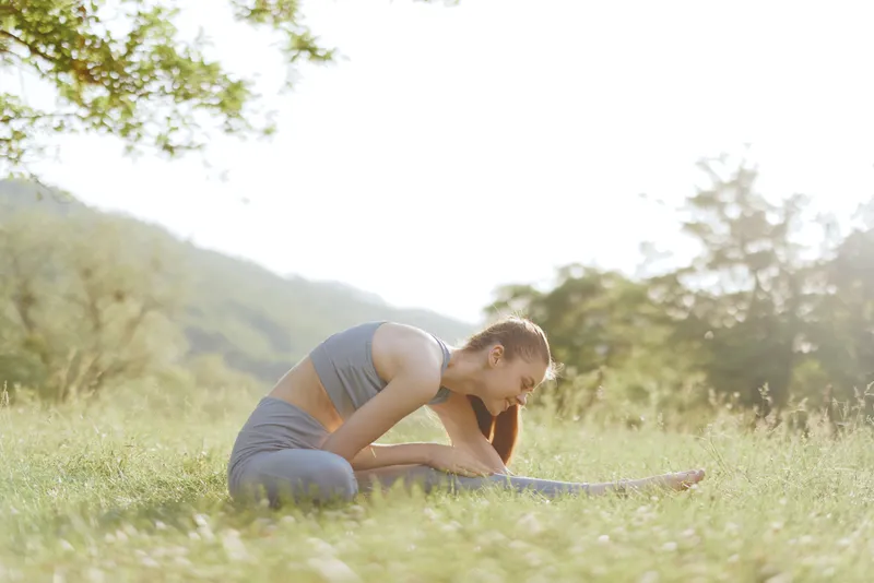 Young woman practicing yoga in a green field, wearing sportswear, showcasing concentration and tranquility in a serene outdoor setting