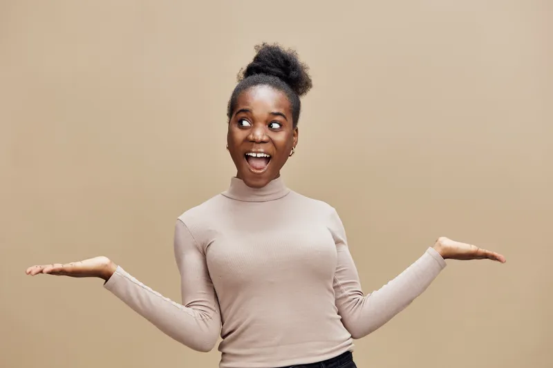 Happy young African woman in a turtleneck, expressing joy and excitement against a neutral beige background, perfect for lifestyle and positivity themes