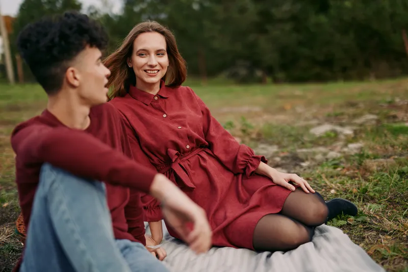 A candid outdoor portrait of a smiling woman and companion seated on a blanket, conveying warmth, natural expressions, authenticity and credibility in an everyday, believable interaction.