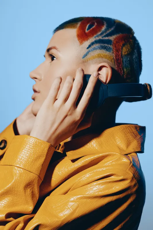 woman with colorful shaved hairstyle talking on phone, wearing yellow textured jacket, modern trendy look and cool expression