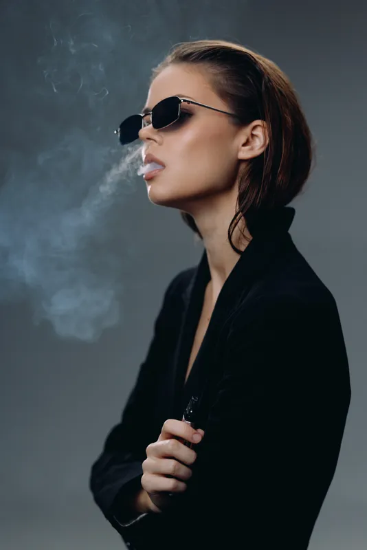 Stylish woman wearing sunglasses smoking vape with cool and confident expression