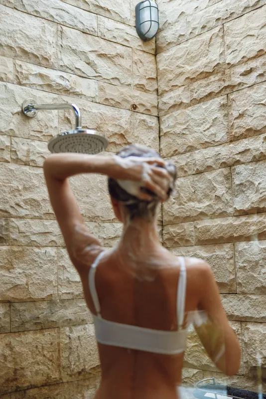 woman showering outdoors with soap, stone wall background, natural light, wet hair, relaxing moment, morning routine, wellness and hygiene