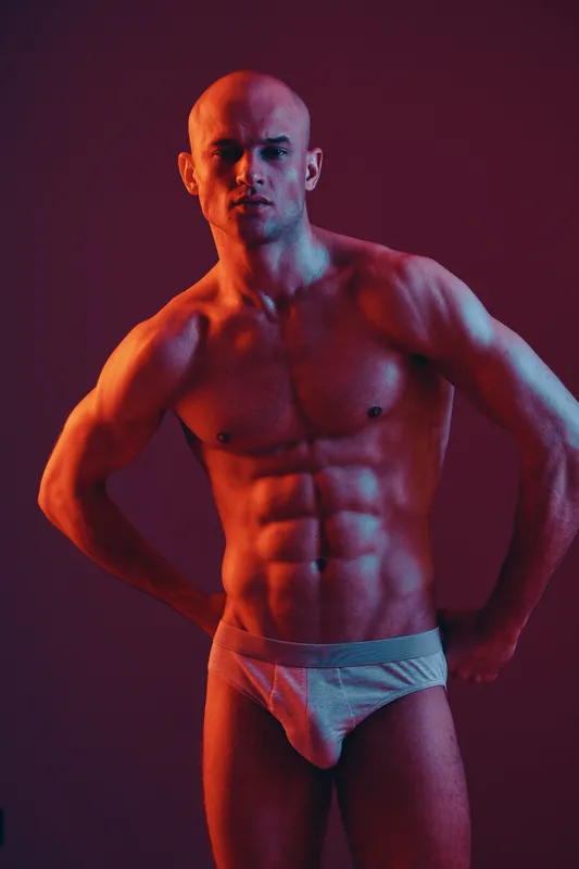 Muscular man posing confidently in dramatic lighting, showcasing his toned physique. The vibrant color palette adds an energetic feel to the image.