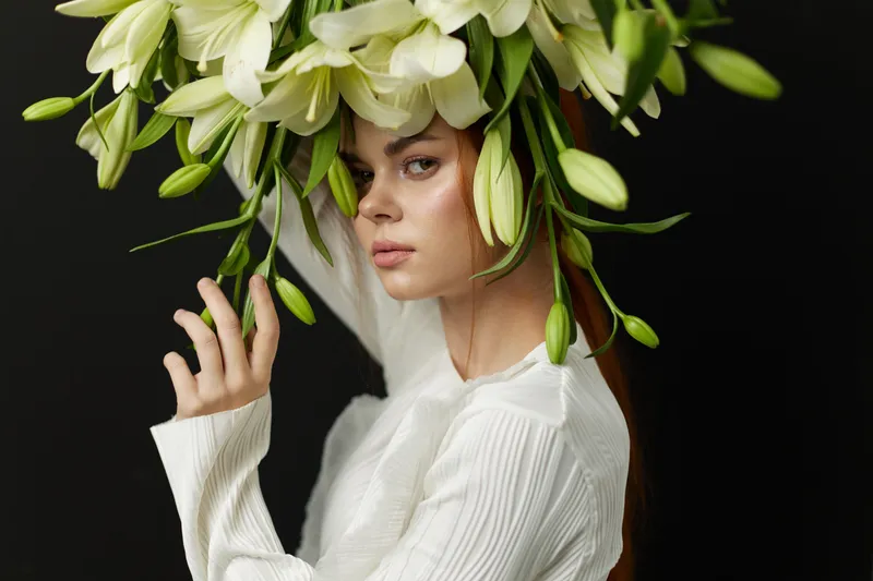Young woman with a floral headdress of white lilies, showcasing a serene expression in a minimalist style against a dark background