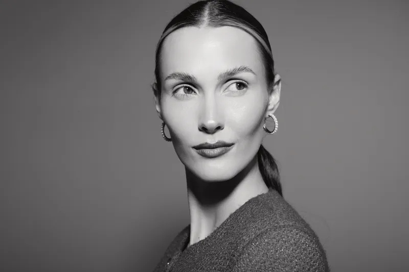 Portrait of a young Caucasian woman with fair skin and slicked back hair looking sideways in black and white studio lighting.