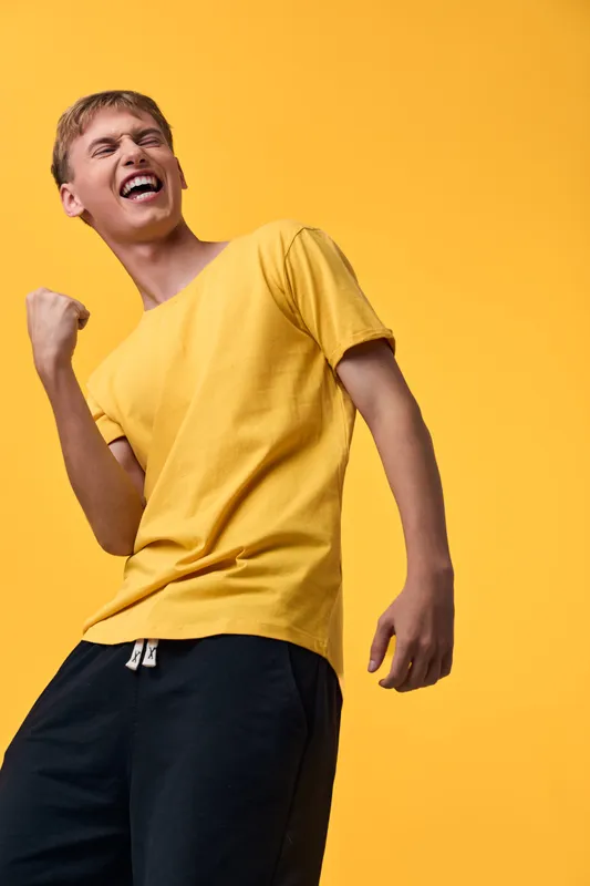 Energetic man in a bright yellow tee expresses triumph with a raised fist against a yellow backdrop, capturing bold enthusiasm, dynamic movement, and casual style for youth, sports, or advertising