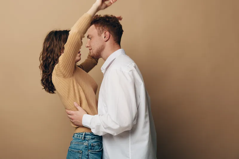 Young couple embraces closely in casual clothes against beige background. Intimate moment shows affection and connection between man and woman in warm, soft lighting.