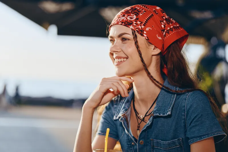 lifestyle woman in modern boho-western denim street style with red bandana, smiling outdoors in warm natural film color lighting, casual and relaxed atmosphere