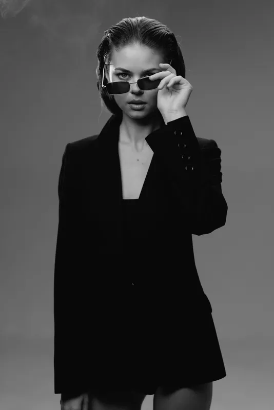 Black and white photo of confident woman wearing sunglasses and a black blazer with a serious expression.