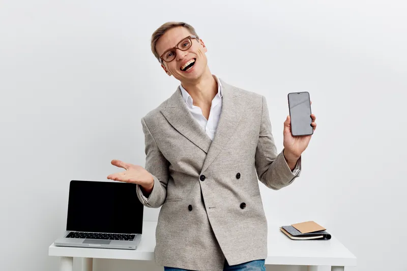 Friendly smiling businesswoman with short hair wearing gray blazer holding smartphone with blank screen standing in modern office studio shot. People lifestyle concept