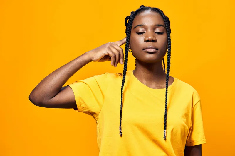 Young Black woman in a yellow t shirt contemplating with eyes closed against a bright yellow background, showcasing inner peace and mindfulness