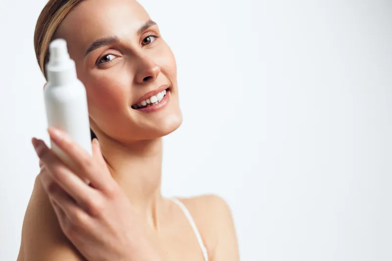 Young woman holding skincare spray bottle, beauty close up on face, serum and hygiene concept, smiling during skincare routine, fresh skin, clean light background