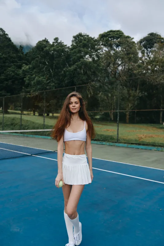 Young female tennis player in white sportswear demonstrating confidence on the court, showcasing athleticism, vibrancy, and a sporty lifestyle