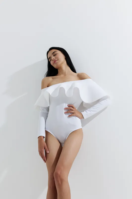 woman sport fitness posing in white off-shoulder bodysuit with long sleeves, graceful posture, smooth skin, and minimalistic bright background, natural light