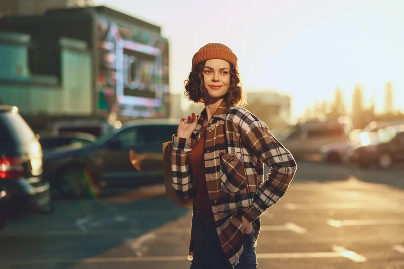 Woman portrait in urban parking lot at golden hour, candid smile and beanie styling conveying authenticity and mindful living, emotional storytelling with warm golden glow.