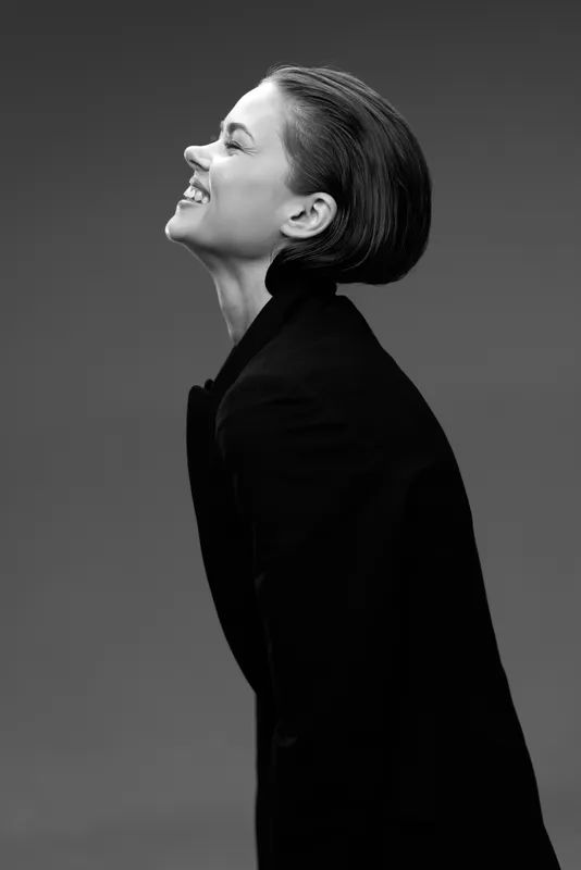 Smiling woman in black coat looking up, black and white portrait with elegant style and positive emotion