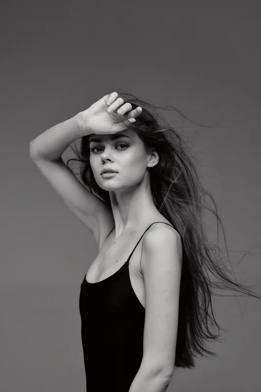 Black and white portrait of a young woman with flowing hair and pensive expression in simple black dress.