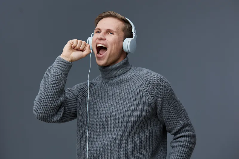 happy caucasian man wear gray sweater headphones singing enjoying music isolated on gray background mental health and gadgets concept