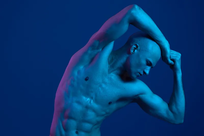 Artistic black and white photograph of a man striking a dynamic pose, showcasing his muscular physique, emphasizing strength and motion in a unique manner.