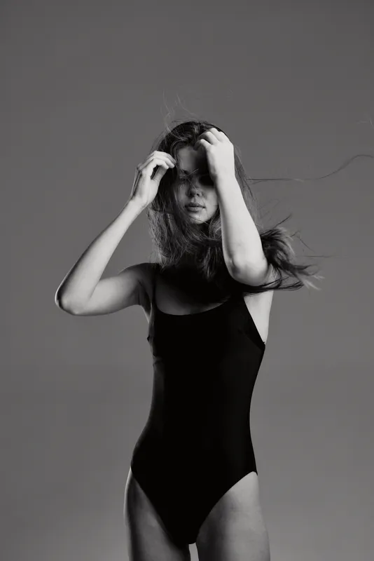 Black and white portrait of a young woman in a black bodysuit with flowing hair and pensive expression