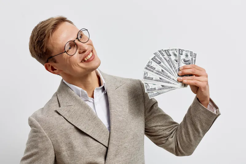 smiling caucasian man holding cash money fan wearing beige blazer glasses digital nomad concept success wealth finance