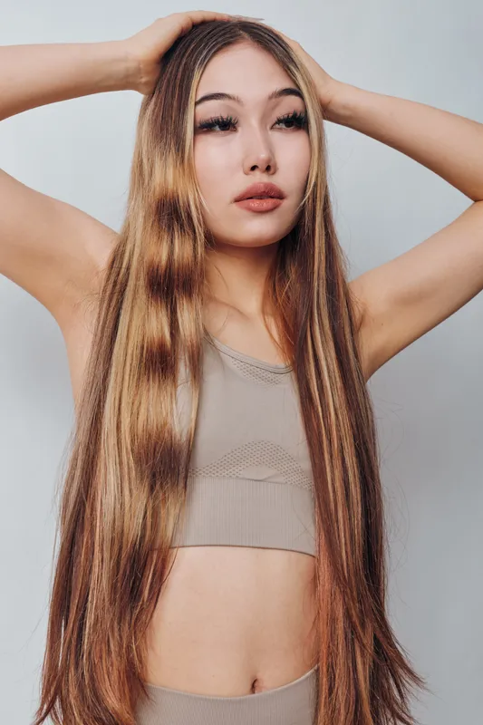Portrait of young woman with long straight hair posing with hand on head wearing beige crop top and leggings on white background, fashion and beauty concept.