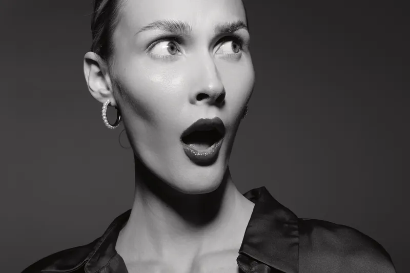 Surprised white woman with light skin looks aside with open mouth in black and white portrait. Concept of shock and unexpected emotion.