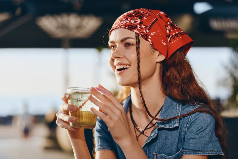Lifestyle woman in modern boho-western denim street style, smiling and holding a drink, natural film color with warm lighting and relaxed mood.