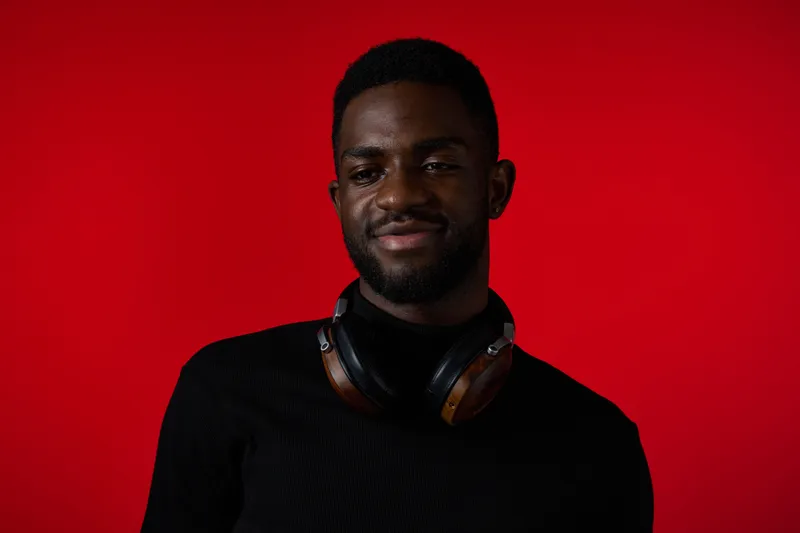 Portrait of a young African man with headphones, smiling against a vibrant red background, showcasing confidence and modern style