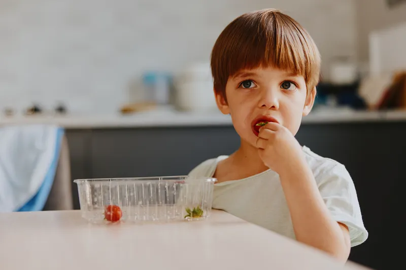 Curious boy enjoying a snack, exploring flavors and colors in a bright kitchen, highlighting healthy eating habits and childhood joy.