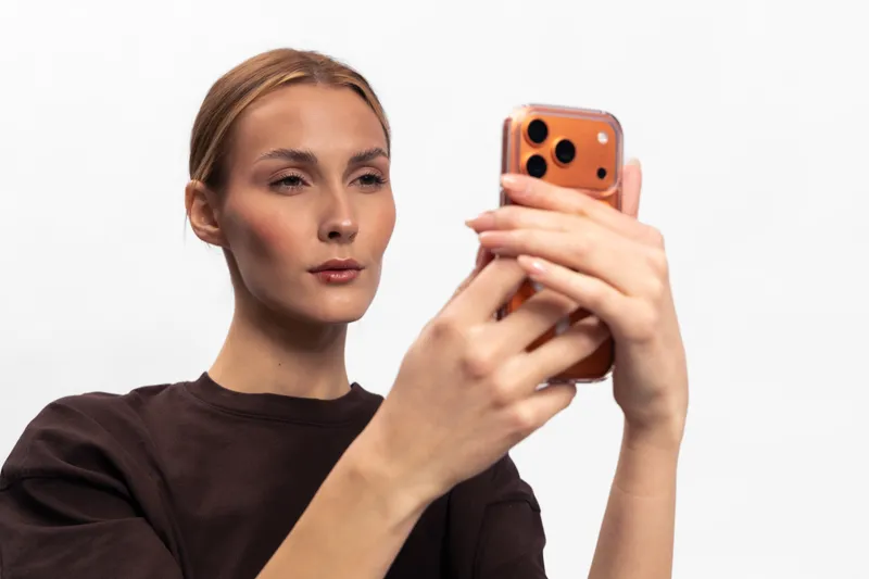 Young woman with tied hair wearing dark sweater holds smartphone taking selfie. Isolated on white background. Concept for social media, technology, communication, and modern lifestyle.