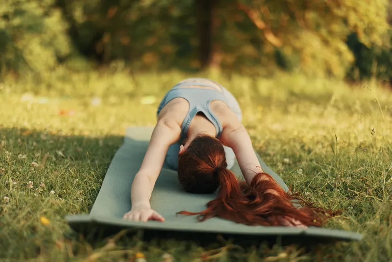 Young woman practicing yoga outdoors in a serene green park, expressing tranquility and focus while stretching in the Child s Pose, surrounded by nature