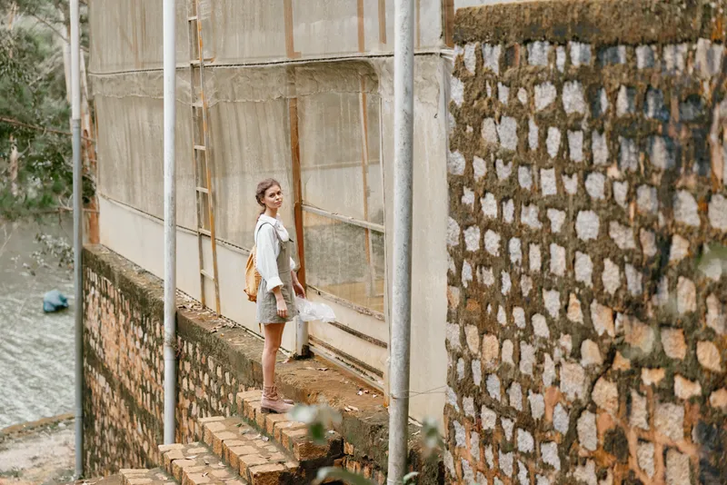 Young woman with a parasol, smiling and standing near a rustic stone wall in a lush green environment, reflecting freedom and serenity during summer